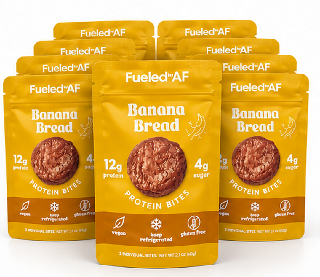 Six yellow and brown stand-up pouches of Fueled+AF Banana Bread Protein Bites arranged in a fan shape on a white background, with the center pouch in front and blue pouches partially visible at the bottom edge.