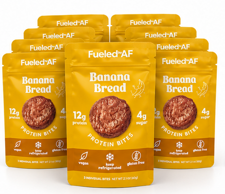 Six yellow and brown stand-up pouches of Fueled+AF Banana Bread Protein Bites arranged in a fan shape on a white background, with the center pouch in front and blue pouches partially visible at the bottom edge.