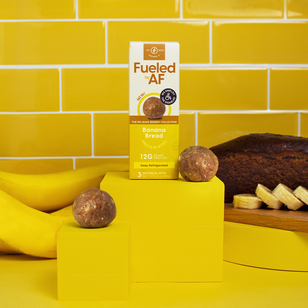 Front of Banana bread box with yellow tile background, with fresh bananas and banana bread.